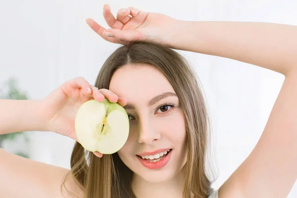 Mujer bella sonriente sosteniendo la mitad de la manzana verde. La chica cierra un ojo con media manzana . —  Fotos de Stock