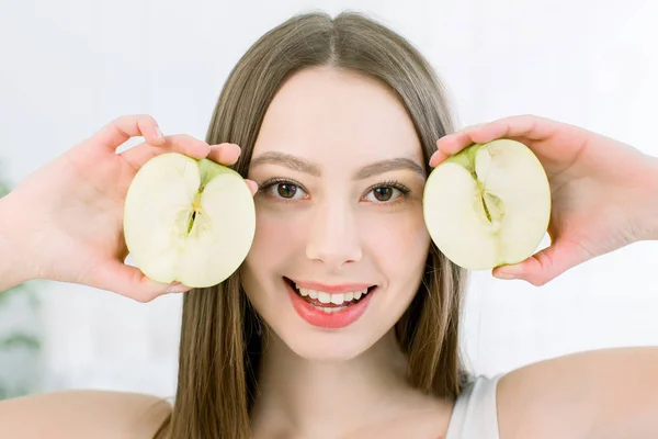 Belleza mujer sonriente con mitades de manzana con la piel sana en la cara posando sobre el fondo claro. Atractiva vitamina fresca. Sesión de estudio . — Foto de Stock