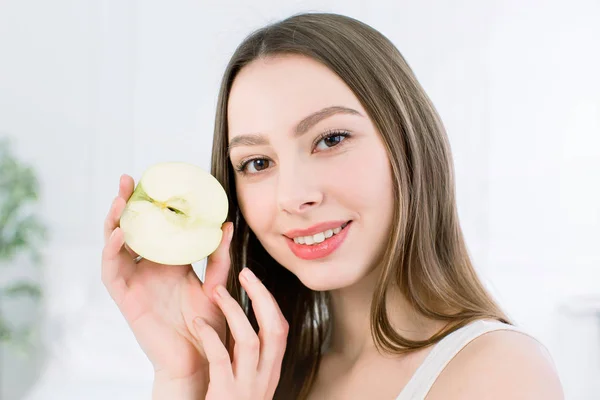 Гарна посмішка, білі міцні зуби. Голова і плечі молодої жінки з білосніжною посмішкою, що тримає зелене яблуко, догляд за зубами . — стокове фото
