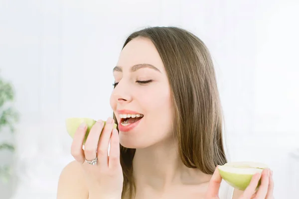 Cara de cerca de una hermosa mujer con una piel limpia y sana, comiendo una manzana, posando y sonriendo. Aislado sobre fondo blanco — Foto de Stock