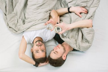 İnsanlar, eşcinsellik, Eşcinsel aile, Eşcinsel ilişkiler kavramı. Birbirlerine sarılma ve çatı katında yatakta yalan sırasında beyaz şarap içme erkek gay çift Oda tasarlanmış