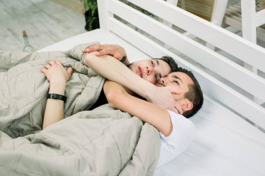 Evde yatakta yatan iki yakışıklı adam. Bir battaniye ışık oda var altında yatan genç gay çift