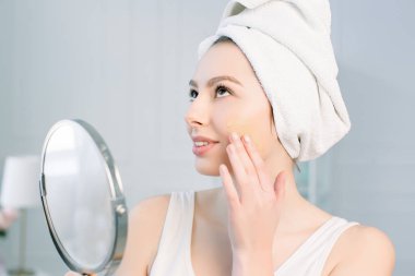 Bir havlu duş, uygulama ton krem Bankası üzerinde aynaya bakmak yüz sonra kız.