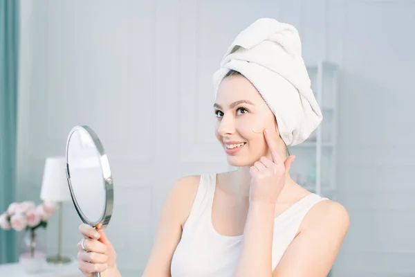 Retrato de atraente mulher branca sorridente no estúdio branco tiro limpar o rosto olhando para o espelho aplicando Foundation On Facial Skin — Fotografia de Stock