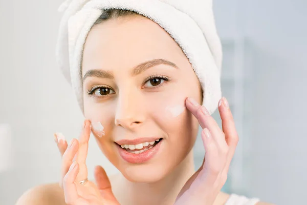 Gyönyörű fiatal nő arcát a fürdőszobában krém alkalmazása. A kezelés a tökéletes bőr koncepció — Stock Fotó