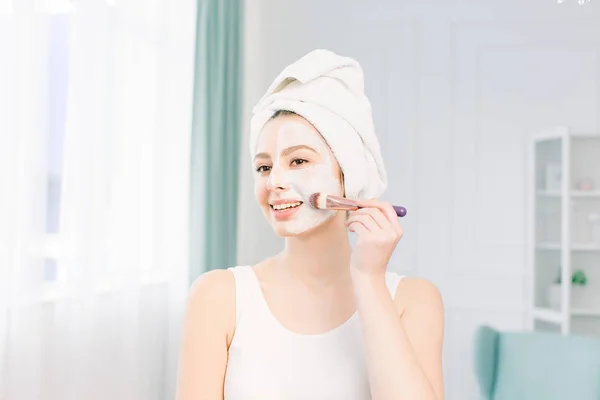Mulher feliz com uma toalha na cabeça aplicar uma máscara de limpeza em seu rosto — Fotografia de Stock