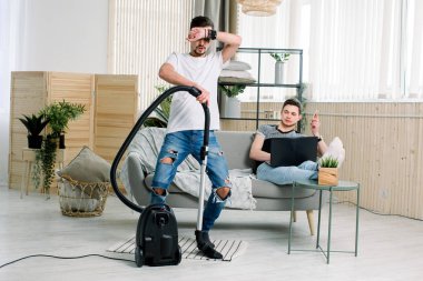 Evde temizlik mutlu gay adam, elektrikli süpürge ile dans ve eğlenmek. Ev işleri, işleri konsepti