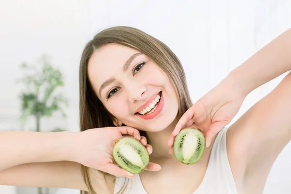 Feliz joven hermosa mujer sosteniendo rebanadas de kiwi cerca de su cara - aislado sobre fondo claro —  Fotos de Stock