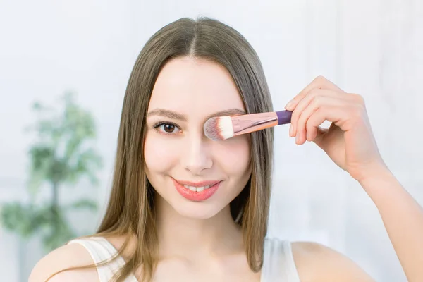 Fechar-se de cara de mulher jovem feliz com a maquilagem escova no fundo leve. Beleza menina conceito de cuidados da pele. Espaço de cópia — Fotografia de Stock