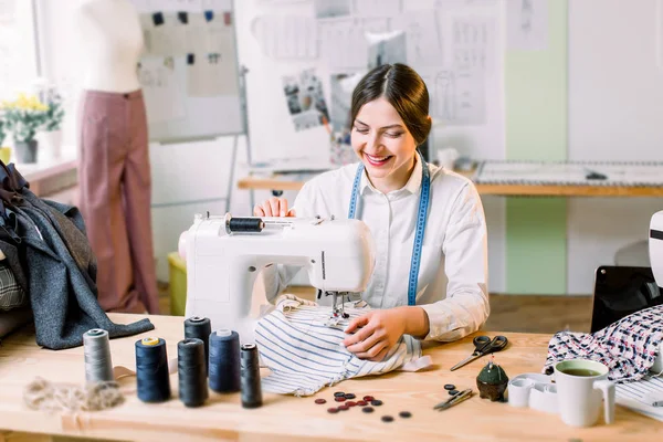 Крупный план портрета молодой женщины-швеи, сидящей и пришивающей швейную машинку. Мода, швейная одежда, хобби шитье как концепция малого бизнеса — стоковое фото