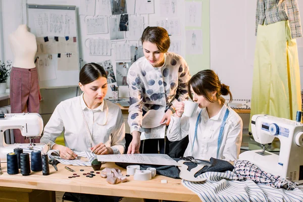 Fashion Design, penjahit, Konsep penjahit. Tiga wanita muda Kaukasia bekerja sama di atelier terang, menyiapkan koleksi pakaian buatan tangan baru — Stok Foto