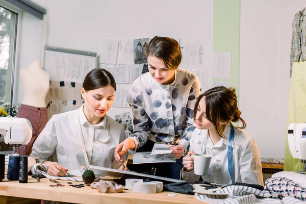 Fashion Design, penjahit, Konsep penjahit. Tiga wanita muda Kaukasia bekerja sama di atelier terang, menyiapkan koleksi pakaian buatan tangan baru — Stok Foto
