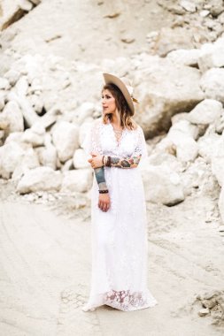 Güzel bir gelin rustik Boho tarzında süslenmiş bir şapka ve uzun beyaz elbise giyen bir kanyon ayakta. Boho çöl düğünü