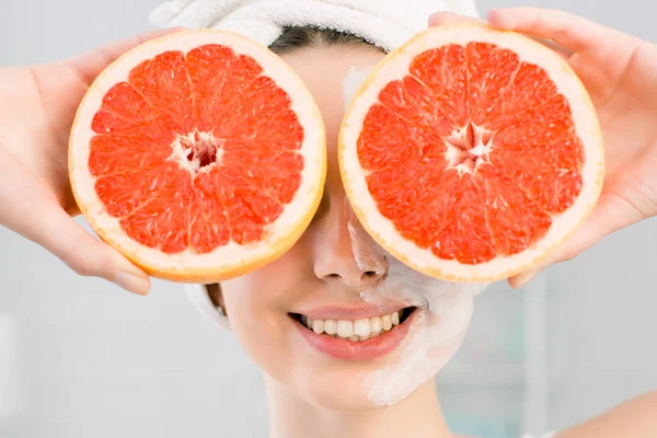 Gadis muda menawan memegang dua bagian dari jeruk di tangan, menutupi matanya. Makanan diet sehat. Kosmetik alami, perawatan kulit, kesehatan, perawatan wajah, konsep kosmologi . — Stok Foto