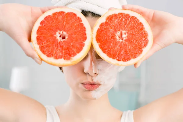 Ung sexig kvinna poserar med kyssar ansikte och skivor av röd grapefrukt i ansiktet på ljus bakgrund. Natur kosmetik, hud vård, Wellness, ansikts behandling, kosmetologikonceptet. — Stockfoto