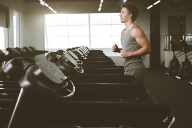 Spor salonunda koşu bandı üzerinde çalışan sporda genç adamın yan görünümü tam uzunluğu. Sağlıklı yaşam tarzı, spor salonunda adam eğitimi. Flare efekti, kopya alanı