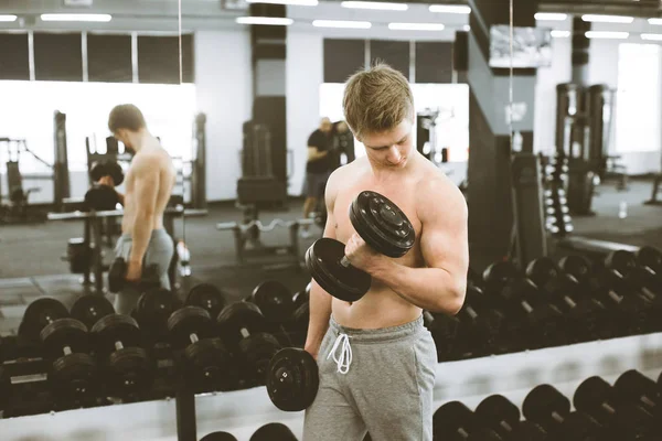 Knappe atletische Guy bodybuilder, het uitvoeren van oefening met halters, in de moderne gym — Stockfoto