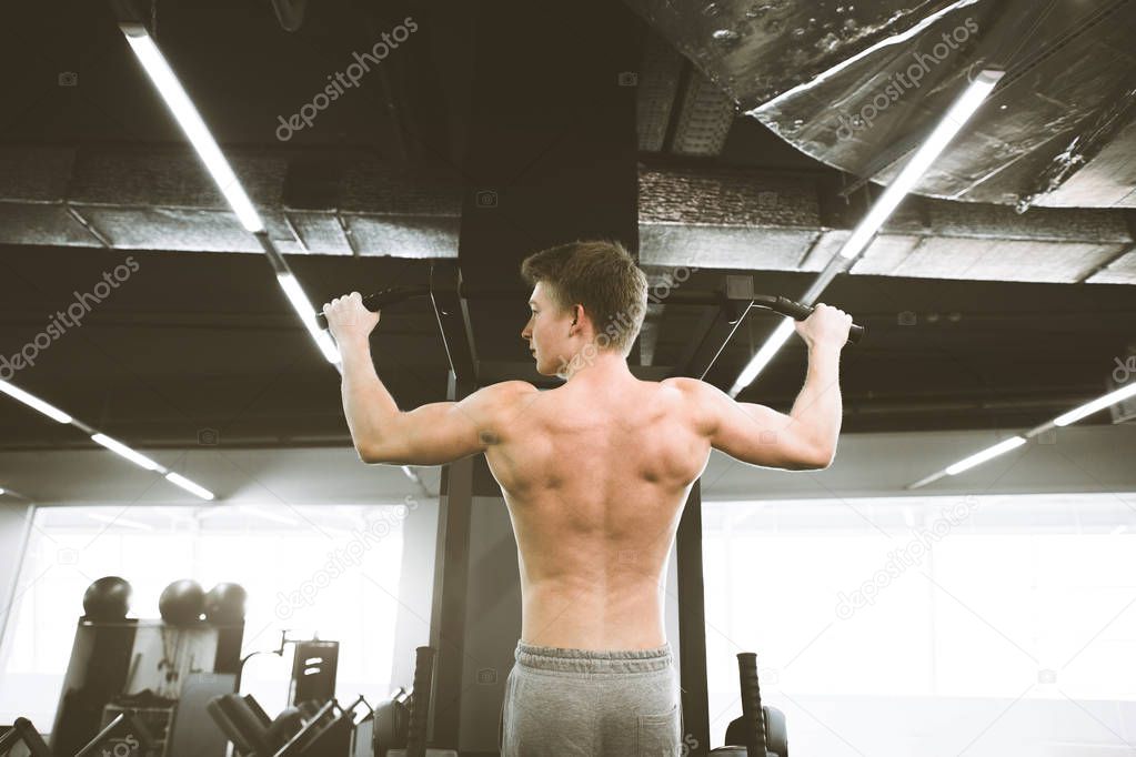 Athlete muscular fitness male model pulling up on horizontal bar in a gym