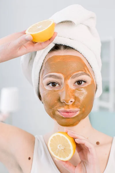 Beauty Skin Care Concept (em inglês). Mulher muito caucasiana em toalha branca com máscara facial de lama marrom no rosto contém frutas cítricas em sua mão no fundo claro. Procedimentos de spa e máscara na pele — Fotografia de Stock