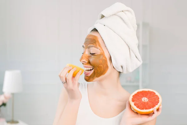 Potret wanita muda cantik dengan masker tanah liat di wajahnya memegang irisan lemon dan jeruk, perawatan wajah — Stok Foto