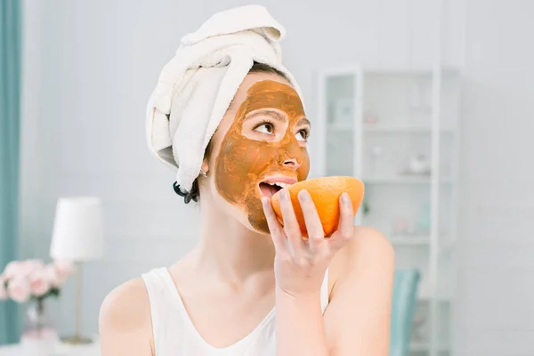 Ritratto di bella giovane donna con maschera di argilla sul suo viso tenendo fette di limone e pompelmo, cura del viso — Foto Stock