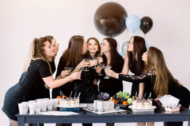 Siyah elbiseler içinde güzel yedi kız birbirleriyle martini gözlük dokunmadan, doğum günü kutluyor, pasta, içecekler, tatlılar ve balonlarla süslenmiş masanın yanında duran