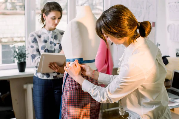 Вид ззаду жінка-виробник одягу, що вимірює манекен зі стрічкою в офісі ательє. Талановитий дизайнер модного магазину, який працює з ескізами для нової колекції одягу. Концепція одягу та шиття — стокове фото
