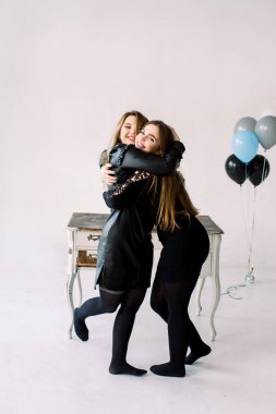 Siyah elbiseler içinde iki genç güzel kadın birlikte hava balonları tutan, dolaplar ile vintage beyaz masa yakınında duran hen veya doğum günü partisi kutluyor, beyaz izole