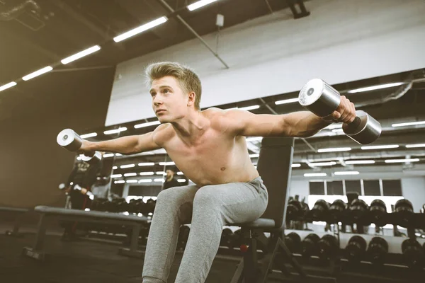 Концентрированный спортсмен во время тренировки в спортзале с гантелями. Поднимает тяжести, тренирует бицепсы. Красивые грудные мышцы — стоковое фото