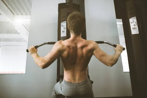 Handsome power athletic man training pumping up back muscles pull up in the gym. Strong bodybuilder trains in the gym, trains his back. Athletic man pumping up muscles workout bodybuilding concept