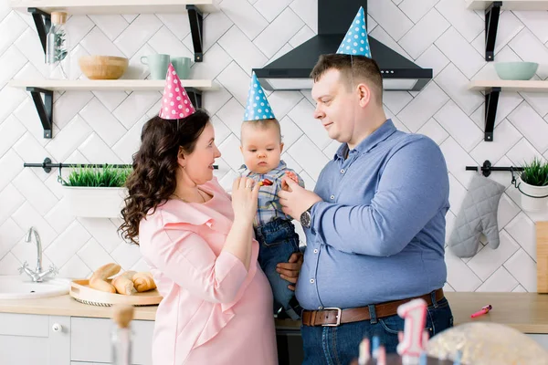 Niño feliz, padre y madre con trompetas y globos en la fiesta de cumpleaños. Joven familia celebrando cumpleaños con un pastel — Foto de Stock