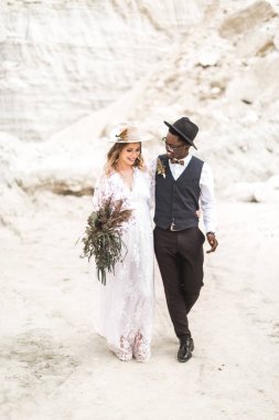 Çöl kanyonunda birlikte yürüyen ve birbirlerine şefkat ve sevgiyle bakan yeni evliler kucaklaşıyor ve el ele tutuşuyorlar. Kanyon arka planda Boho ve rustik şık düğün