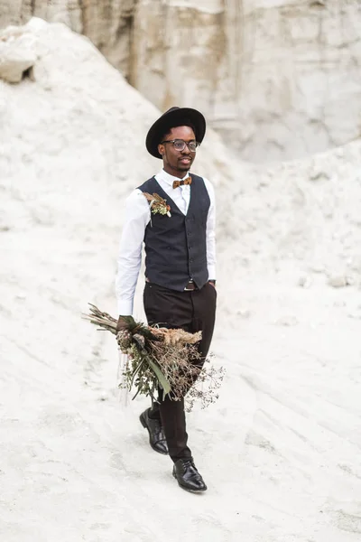 Zwarte Afro Amerikaanse bruidegom in stijlvolle Blask pak en hoed wandelen in Desert Sand Canyon tegen prachtige landschap. Canyon bruiloft, Desert Love Story — Stockfoto