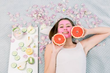 Hafif arka planda yüz maskesi ve greyfurt yarıları ile güzel genç kadın