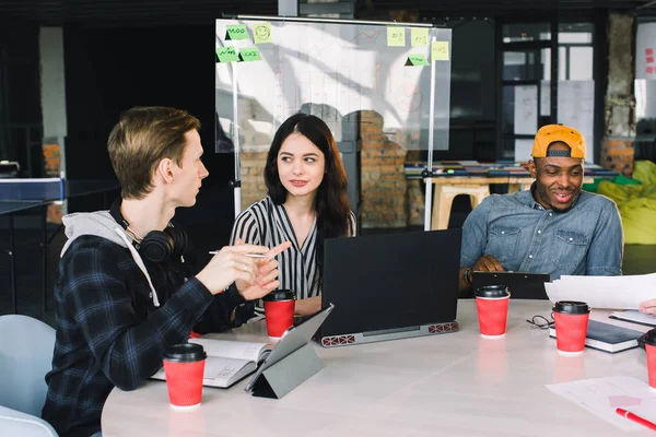 Group of diverse college students sitting together and studying on campus. Friends or business colleagues talking and discussing work ideas in office during informal meeting. Concept of team startup