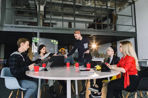 Vidám multifaji férfi és női kollégák szórakoztunk során együttműködési munkafolyamat coworking Office, kreatív sokszínűség csoportja a tervezők részesedése ötleteket és nevetve ül az asztalnál együtt — Stock Fotó