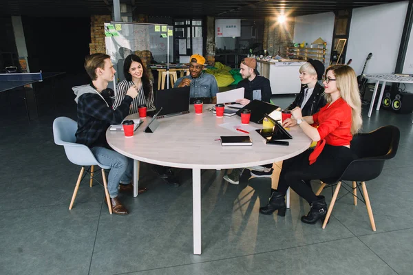 Glada multirasistiska manliga och kvinnliga kollegor ha kul under samarbetet arbetsflöde i Coworking Office, kreativ mångfald grupp av designers dela idéer och skratta sitter vid bordet tillsammans — Stockfoto