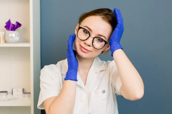 Ritratto di una bella dottoressa sorridente che indossa dei guanti. impiegato medico. Cosmetologo prima della procedura anti invecchiamento per il suo cliente. Medicina estetica, cura della pelle e cosmetologia . — Foto Stock