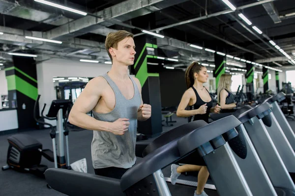 Picture of people running on treadmill in gym. Handsome trainer and two young women on the treadmill in gym. Fitness concept — Stock Photo, Image