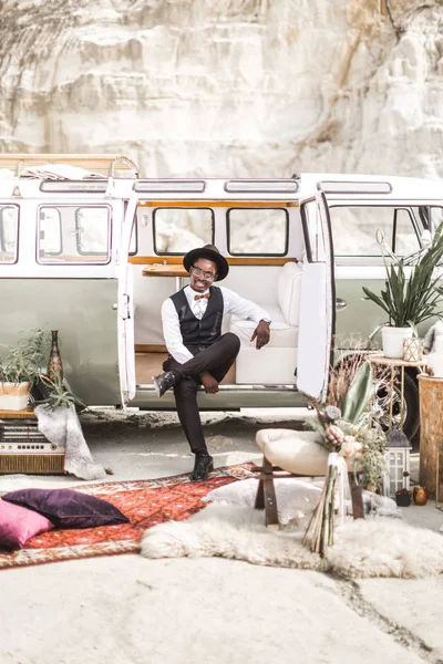 Knappe lachende elegante Afro-Amerikaanse man in pak en hoed zittend in retro stijl minivan — Stockfoto