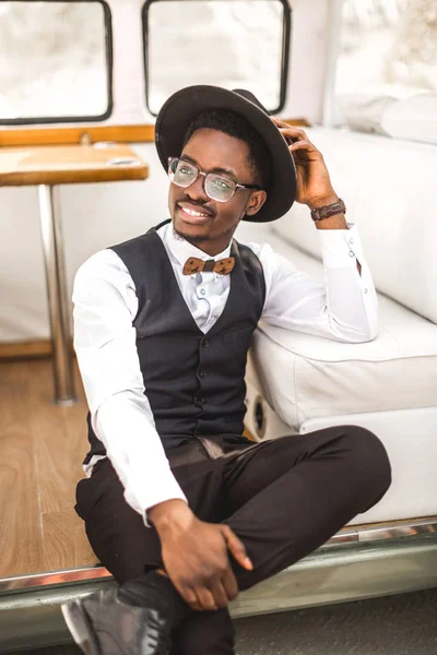 Retrato de cerca del hombre africano guapo en traje elegante y sombrero sonriendo mientras está sentado en minivan de autobús retro en el cañón — Foto de Stock