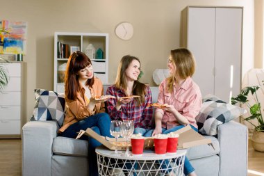 Evde pizza yiyen üç güzel genç kadın. Fast Food yemek. Mutlu güzel arkadaşlar gülüyor, evde pizza yiyor parti. Birlikte yemek yiyor, yemek yiyor. Eğlence, Dostluk