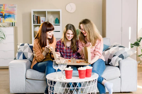 Drie vrouwen vrienden het eten thuis. Foto van vrolijke verrast meiden die thuis een feestje vieren, kartonnen doos openen met pizza. — Stockfoto