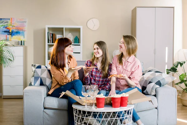 Three beautiful young women eating pizza at home. Eating Fast Food. Happy Beautiful Friends Laughing, Eating Pizza At Home Party. Woman Having Dinner Together, Enjoying Meal. Leisure, Friendship