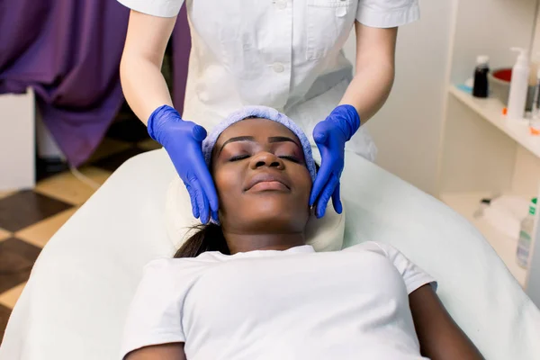 Вид на молоду африканську жінку, що розслабляє на масажне ліжко отримувати масаж обличчя в салоні краси. — стокове фото