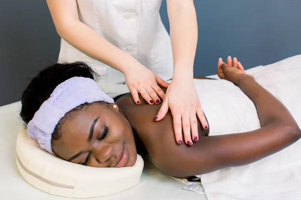 Attractive african girl having massage relaxing in spa salon. Closed eyes. Closeup of happy african woman receiving back massage at salon spa — Stock Photo, Image