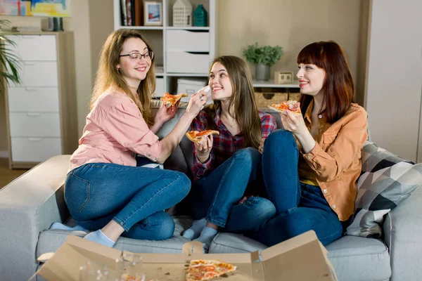 Waktunya makan pizza. Tiga wanita cantik tersenyum makan pizza, bersenang-senang bersama di ruang makan rumah. Persahabatan, makanan, konsep gaya hidup — Stok Foto