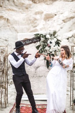 Komik hippi Düğün çift boho tarzı giyinmiş kanyon açık havada düğün kemer önce kalıyorum ve birbirlerine parmaklarını gösteren. Boho düğünü. boho tarzı.