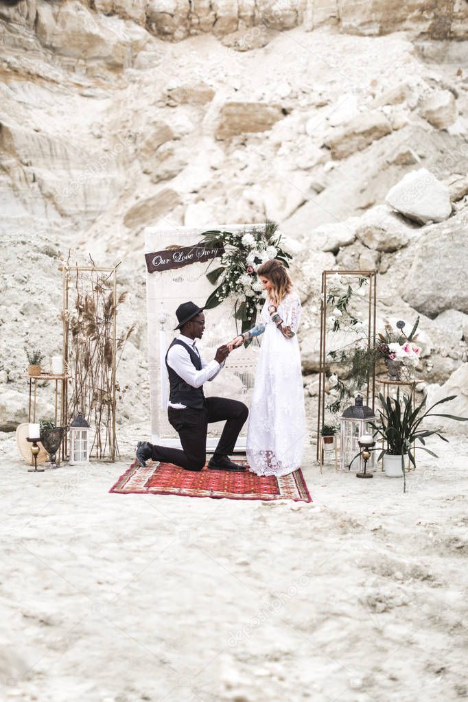 Pareja de boda vestida en estilo boho se quedan ante el arco de la