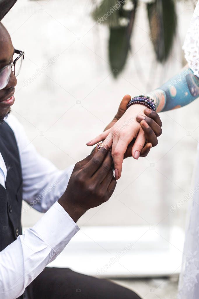 African groom wears wedding ring on the finger of Caucasian bride. Marriage closeup. boho wedding. boho style. happy. happiness. dream.